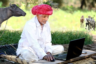 Farmer sitting with a computer and animal in a farm