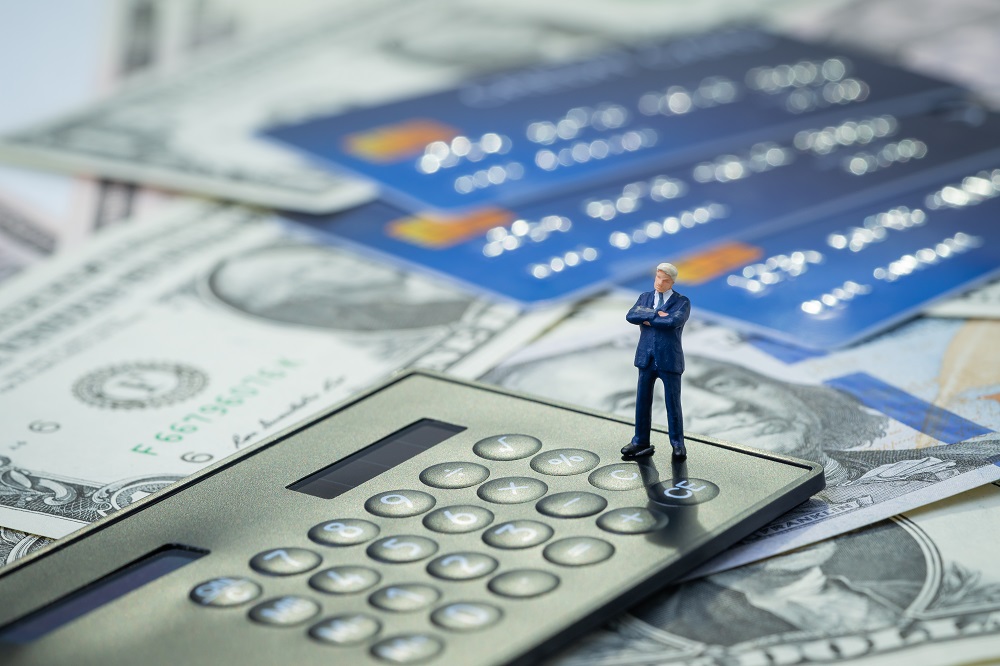 Little business man standing on a calculator with credit cards and money on the background