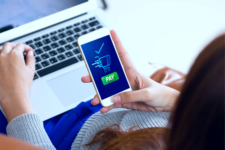 Woman with a laptop and a phone with pay image on screen