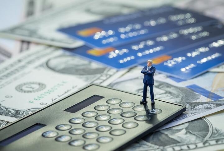 Little business man standing on a calculator with credit cards and money on the background