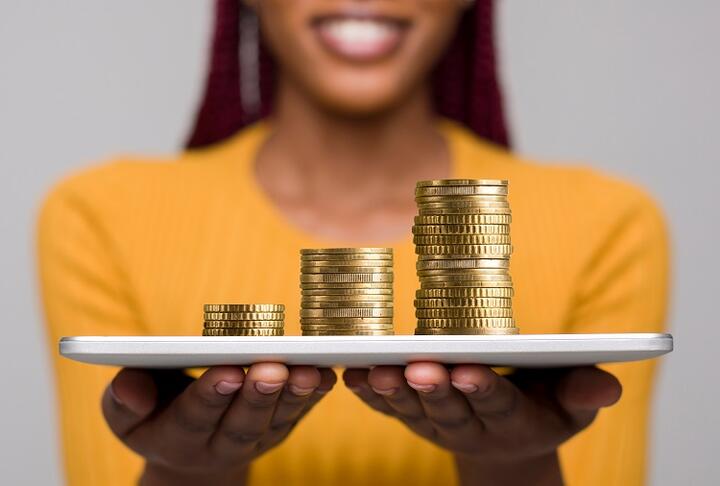 African woman holding a tablet with piles of coins