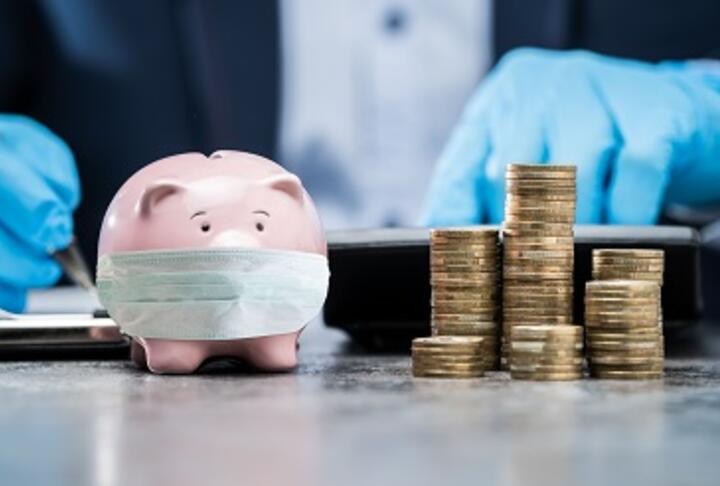 piggy bank with mask and man in background on a suit with gloves and pile of coins