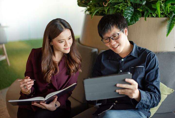 Woman Entrepreneur in a suit, taking notes, with man watching at a tablet