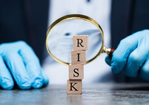 Hands with gloves and a magnifier looking at a pile of cubes with letters RISK